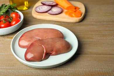 Photo of Plate with fresh raw pork kidneys on wooden table