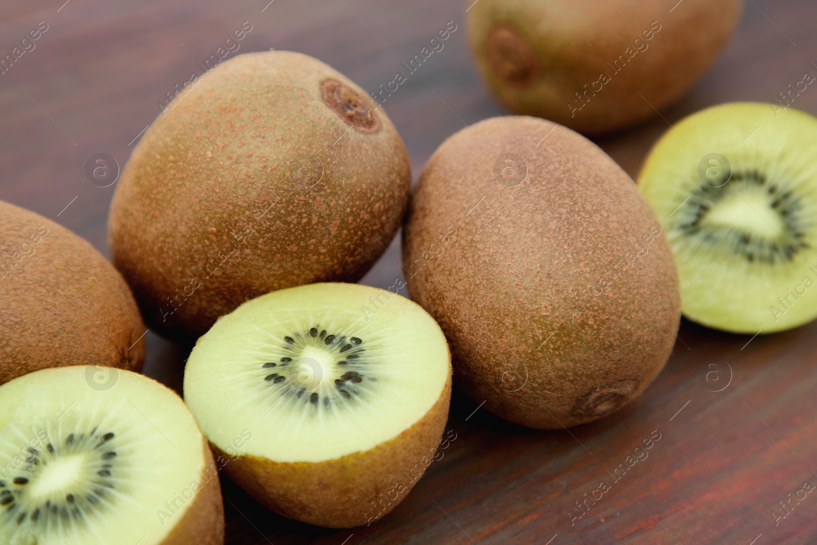 Photo of Whole and cut ripe yellow kiwis on wooden table, closeup