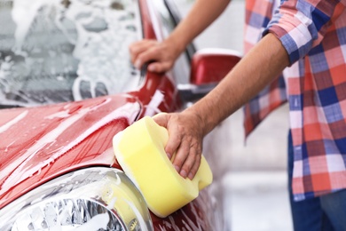 Man washing red auto with sponge at car wash, closeup