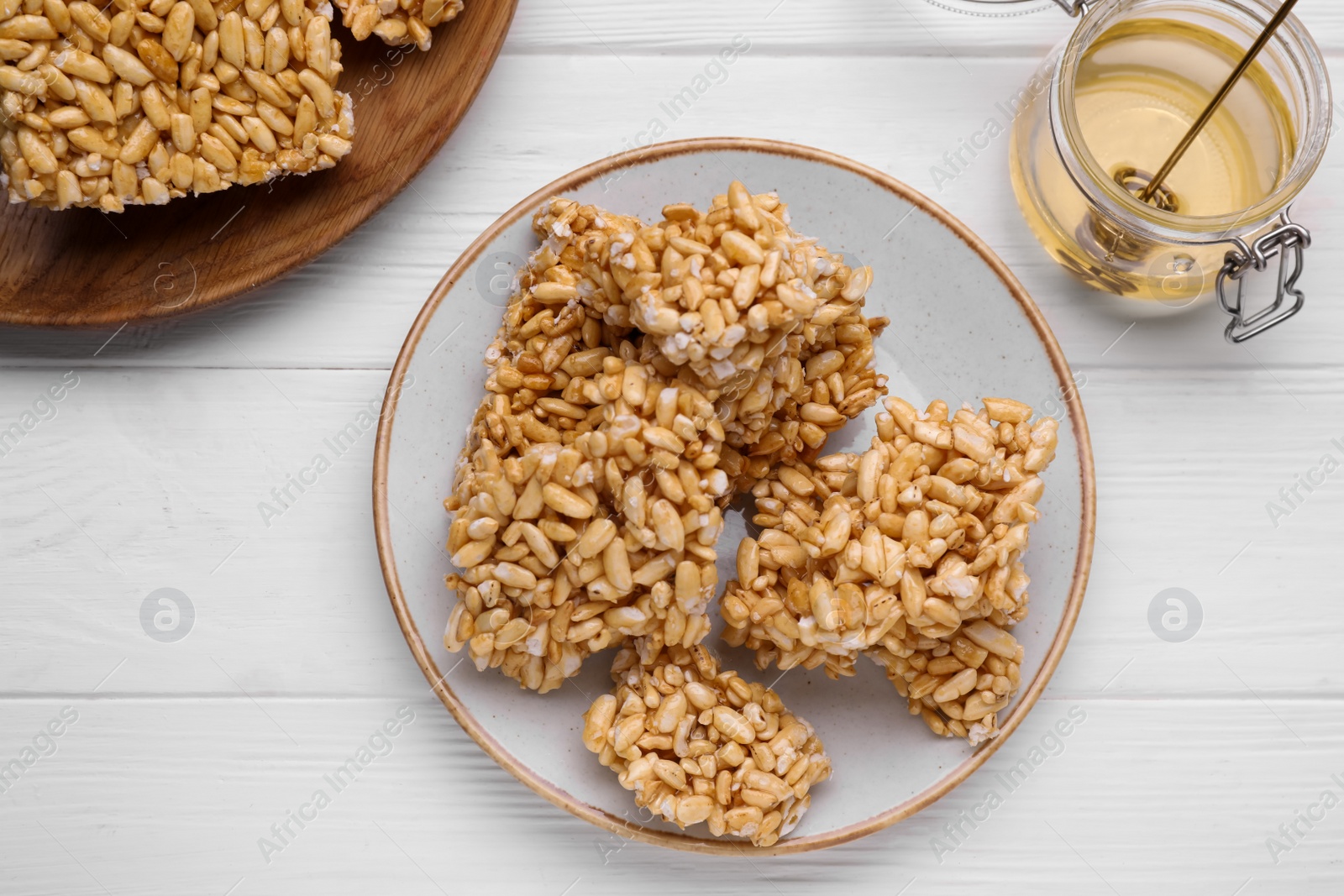 Photo of Puffed rice bars (kozinaki) and honey on white wooden table, flat lay