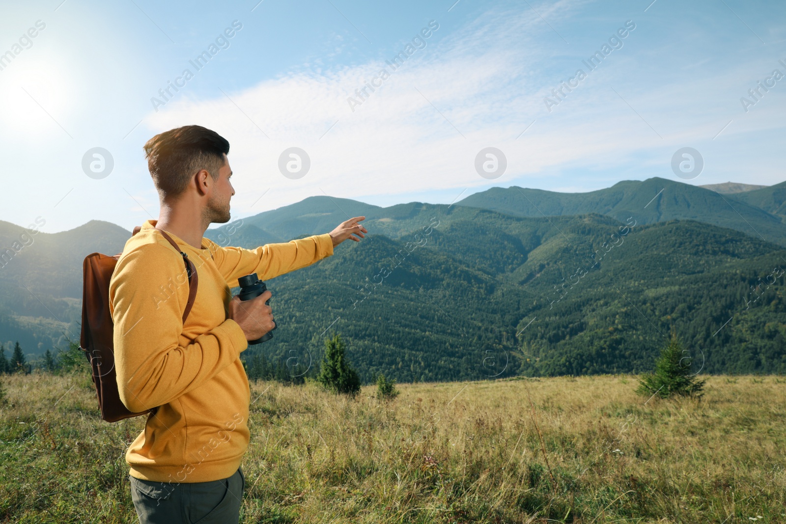 Photo of Man with binoculars in mountains on sunny day, space for text