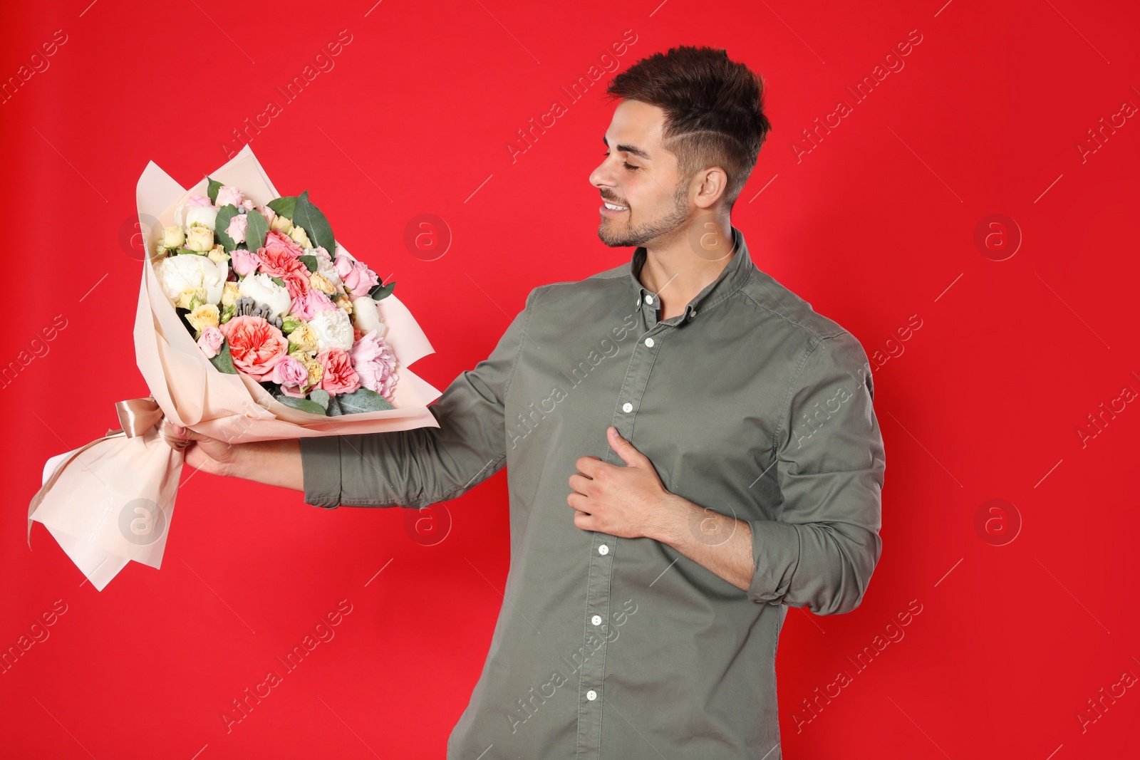 Photo of Young handsome man with beautiful flower bouquet on red background