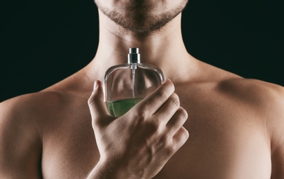 Handsome man using perfume on black background, closeup