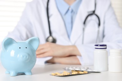 Photo of Doctor with piggy bank and pills at white table, closeup