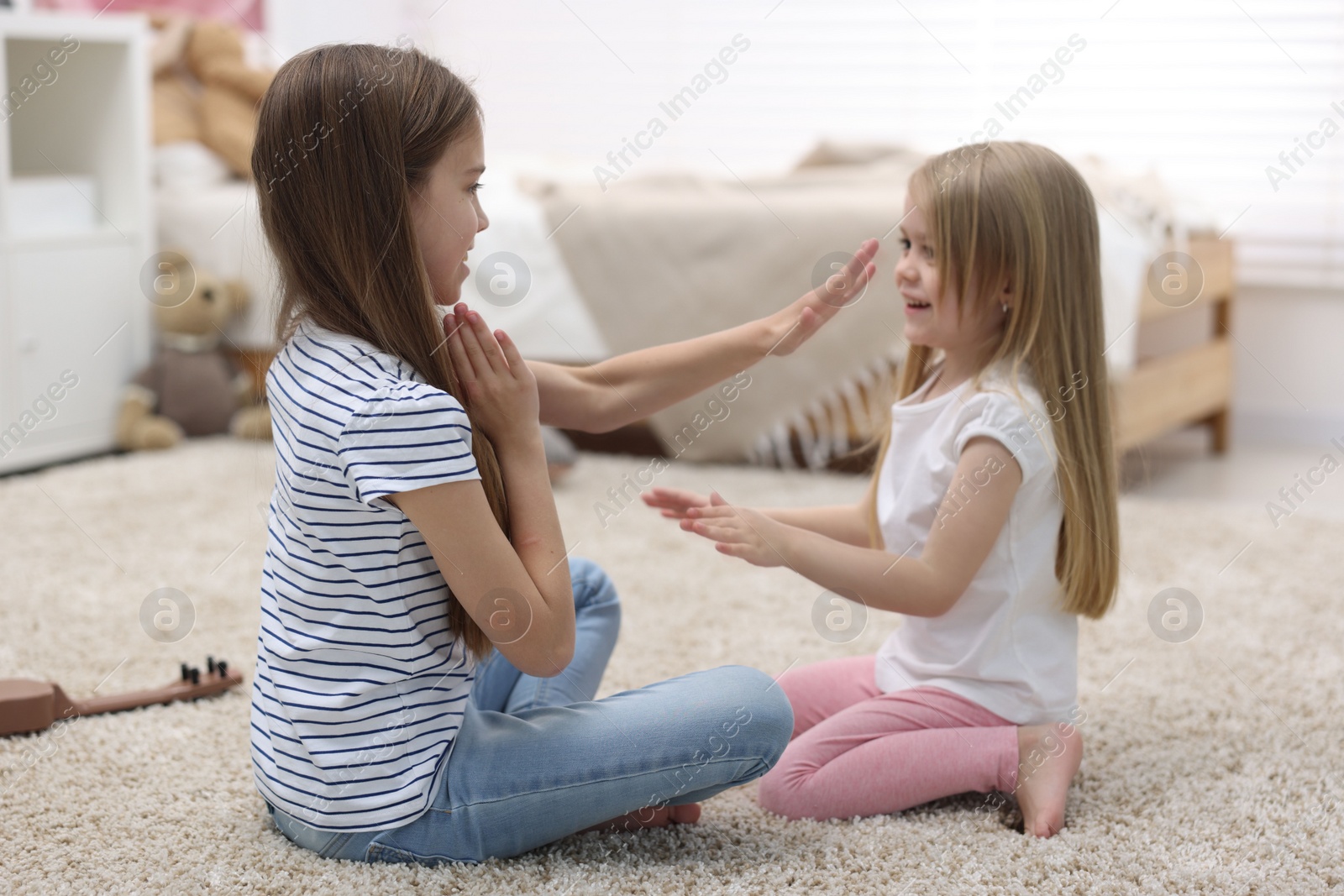 Photo of Cute little sisters playing clapping game with hands at home