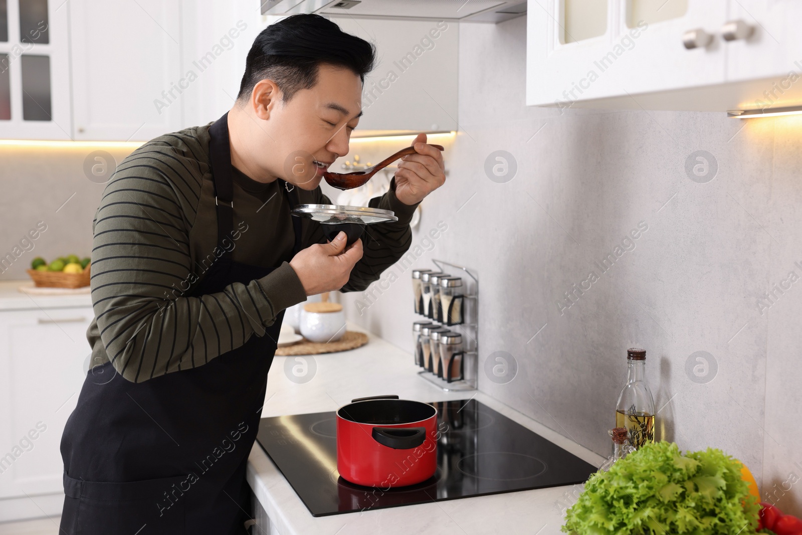 Photo of Cooking process. Man tasting dish in kitchen