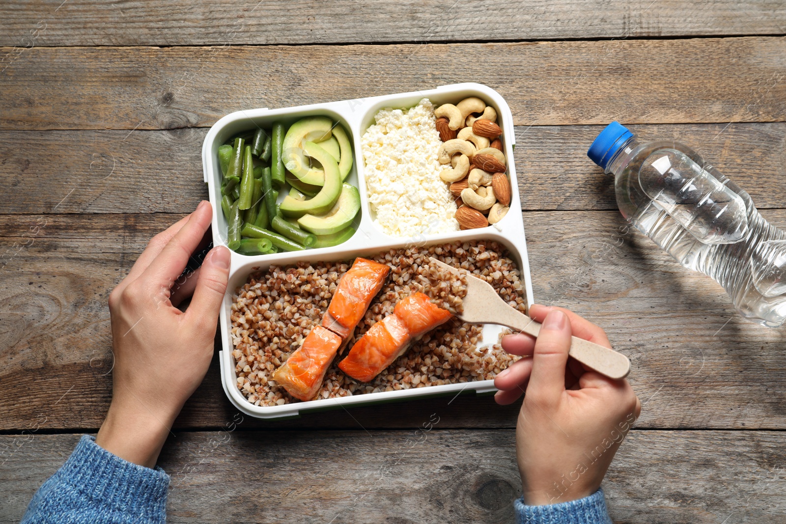 Photo of Woman eating natural protein food from container at table, top view