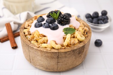 Photo of Tasty granola, yogurt and fresh berries in bowl on white tiled table, closeup. Healthy breakfast