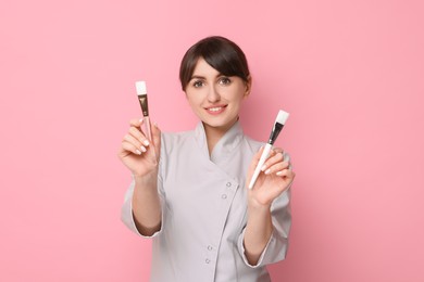 Photo of Cosmetologist with cosmetic brushes on pink background