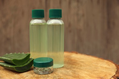 Photo of Bottles of cosmetic products and sliced aloe vera leaves on wooden stump. Space for text