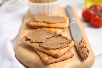 Photo of Crispy crackers with delicious meat pate and knife on wooden board, closeup