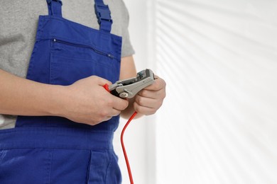 Photo of Professional electrician in uniform stripping wiring indoors, closeup. Space for text