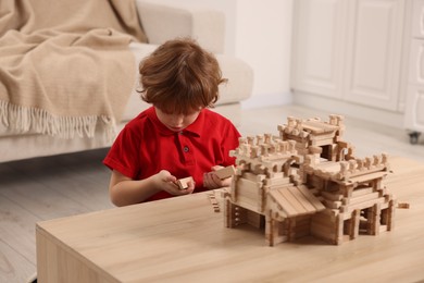 Photo of Little boy playing with wooden castle at table in room. Child's toy