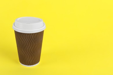Photo of Brown paper cup with plastic lid on yellow background, space for text. Coffee to go
