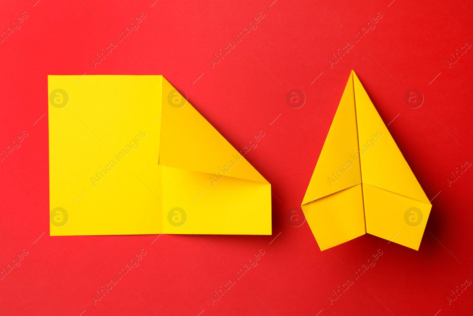 Photo of Handmade yellow plane and folded piece of paper on red background, flat lay