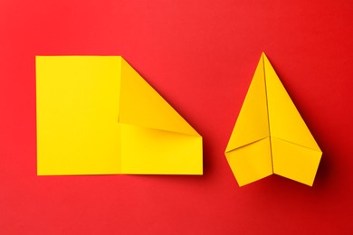 Photo of Handmade yellow plane and folded piece of paper on red background, flat lay