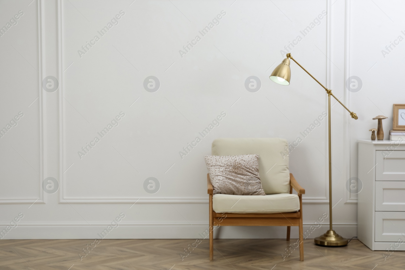 Photo of Stylish room interior with lamp, chest of drawers and armchair near white wall. Space for text