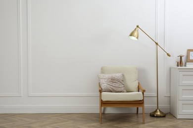 Photo of Stylish room interior with lamp, chest of drawers and armchair near white wall. Space for text