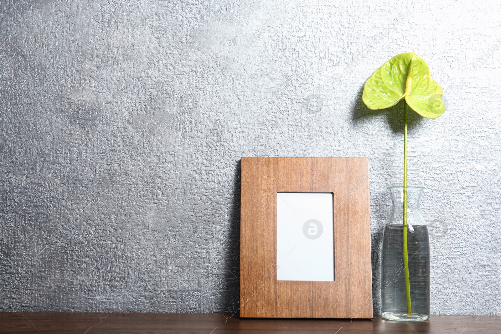 Photo of Blank frame and vase with flower on table near color wall. Mock up for design