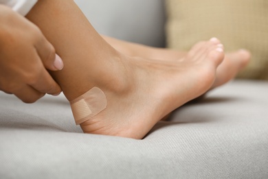 Photo of Woman with adhesive bandage on heel indoors, closeup