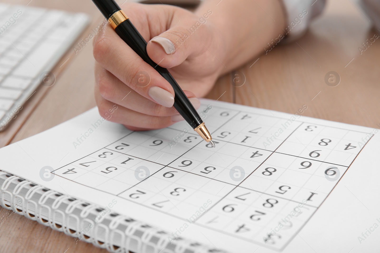 Photo of Woman solving sudoku puzzle at table, closeup