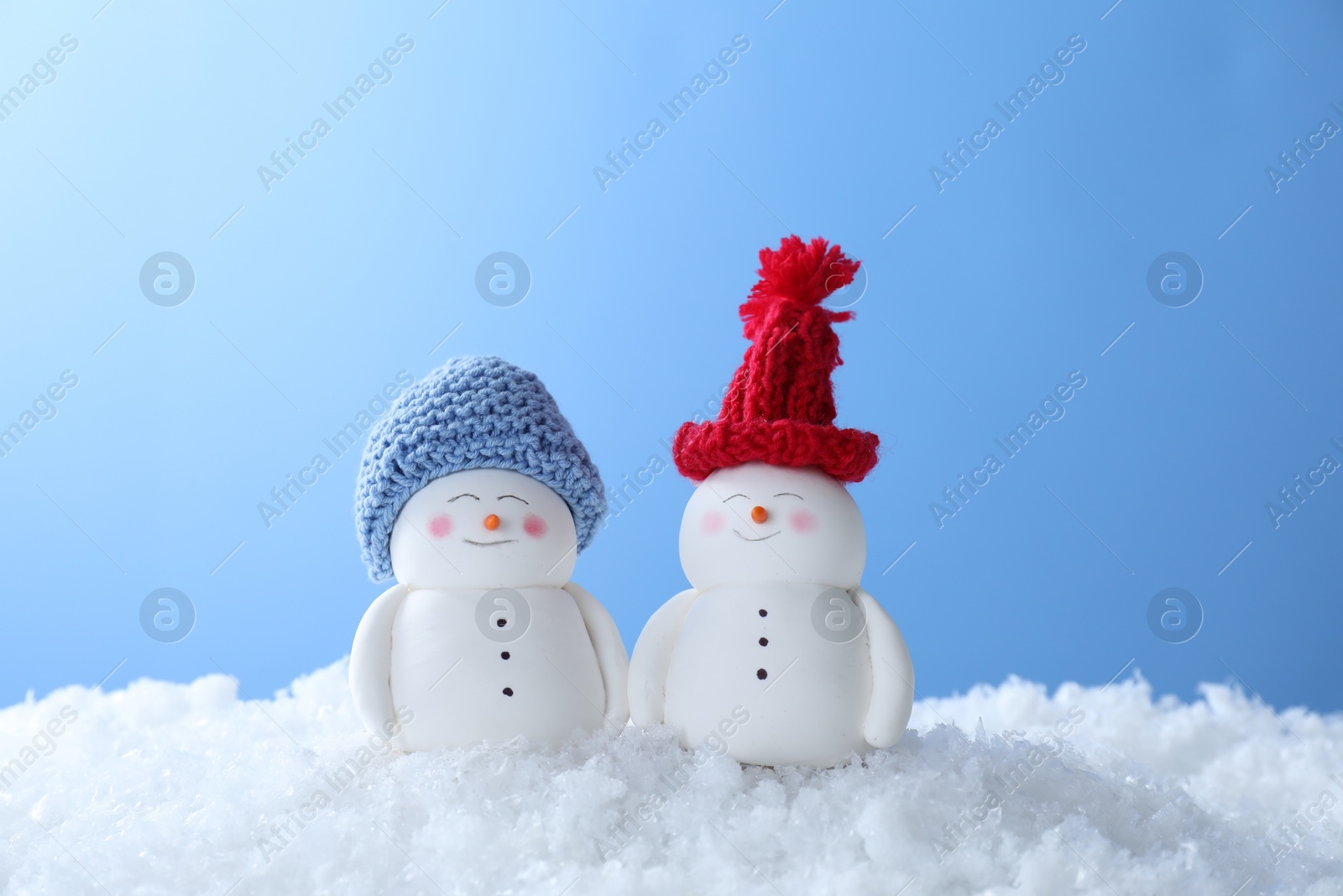 Photo of Cute decorative snowmen on artificial snow against light blue background