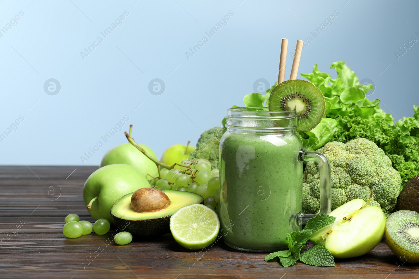 Photo of Green smoothie in mason jar and fresh ingredients on wooden table. Space for text