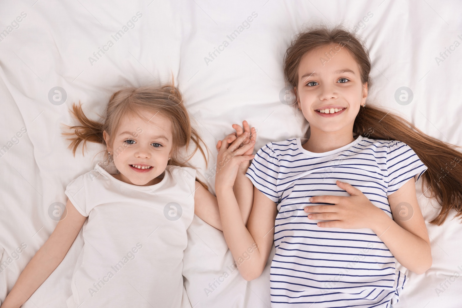 Photo of Cute little sisters on bed, top view