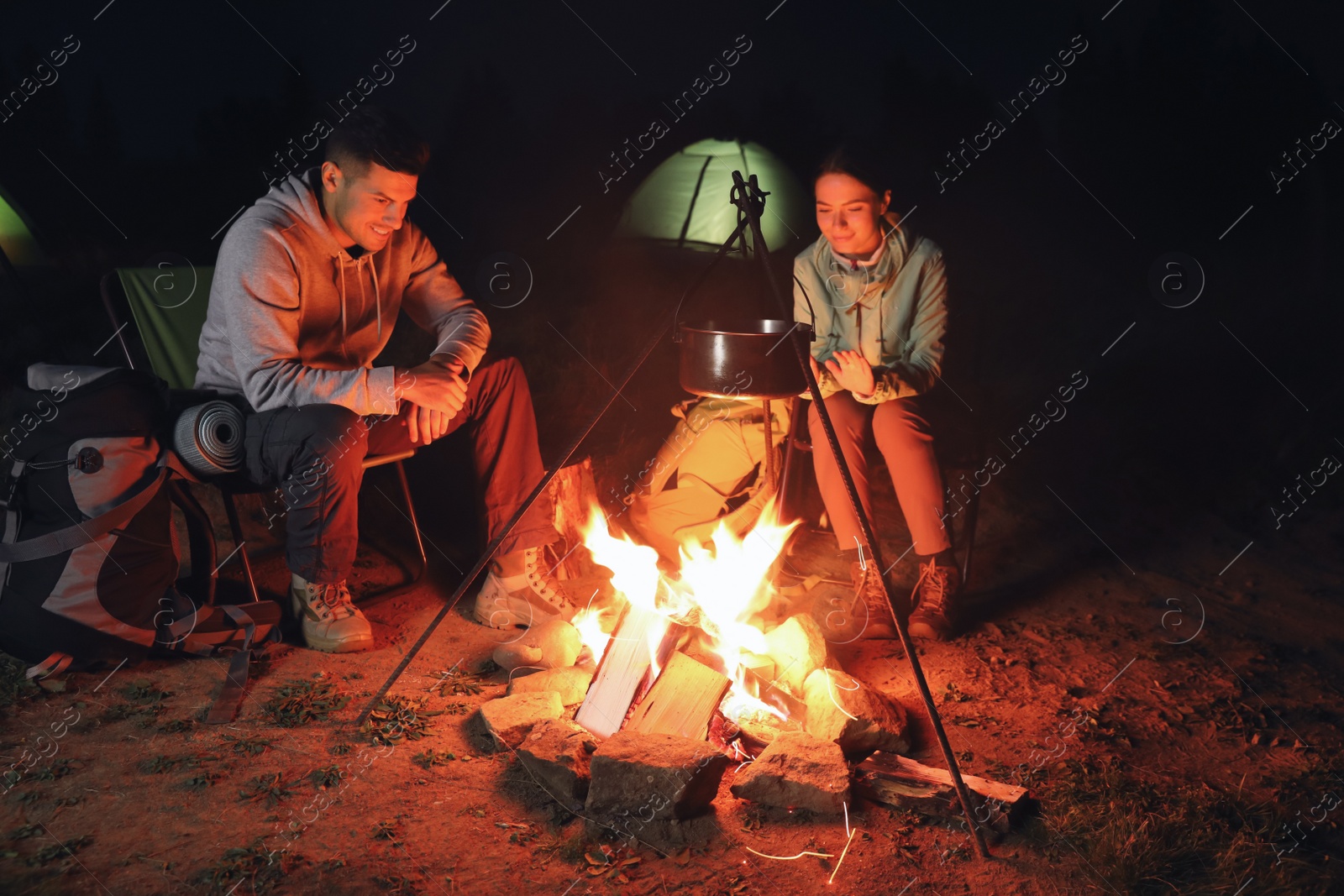 Photo of Couple near bonfire outdoors in evening. Camping season