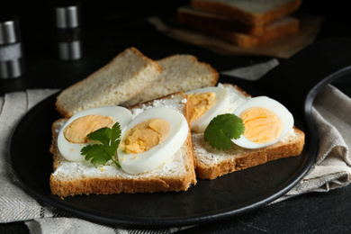 Photo of Tasty sandwiches with boiled eggs on slate board, closeup