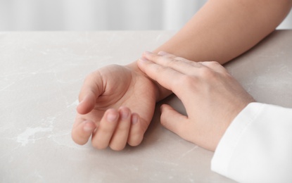 Photo of Doctor checking patient's pulse on table, closeup