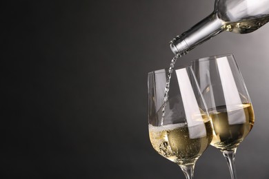 Photo of Pouring white wine into glass against grey background, closeup. Space for text