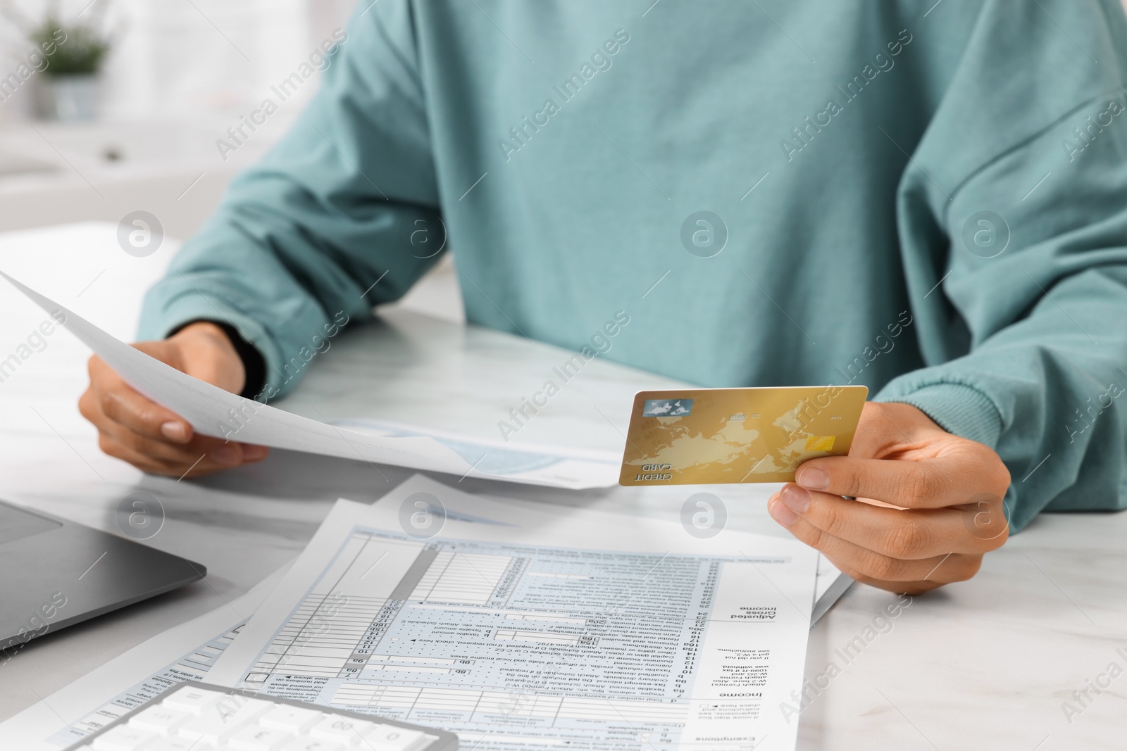 Photo of Woman with credit card doing taxes at table indoors, closeup
