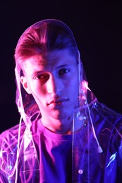 Photo of Young man wearing clear coat on dark background in neon lights