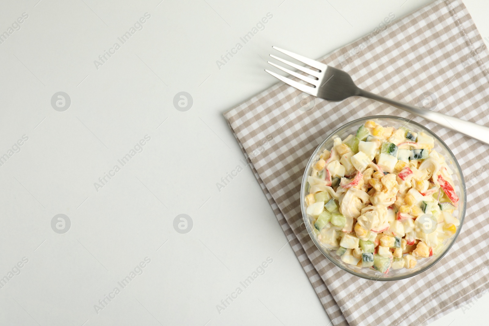 Photo of Delicious salad with fresh crab sticks in glass bowl on white table, top view