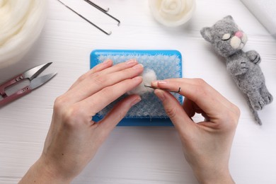 Photo of Woman felting toy from wool at white wooden table, top view