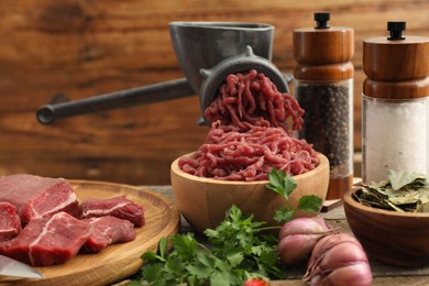 Photo of Manual meat grinder with beef, parsley and spices on wooden table, closeup