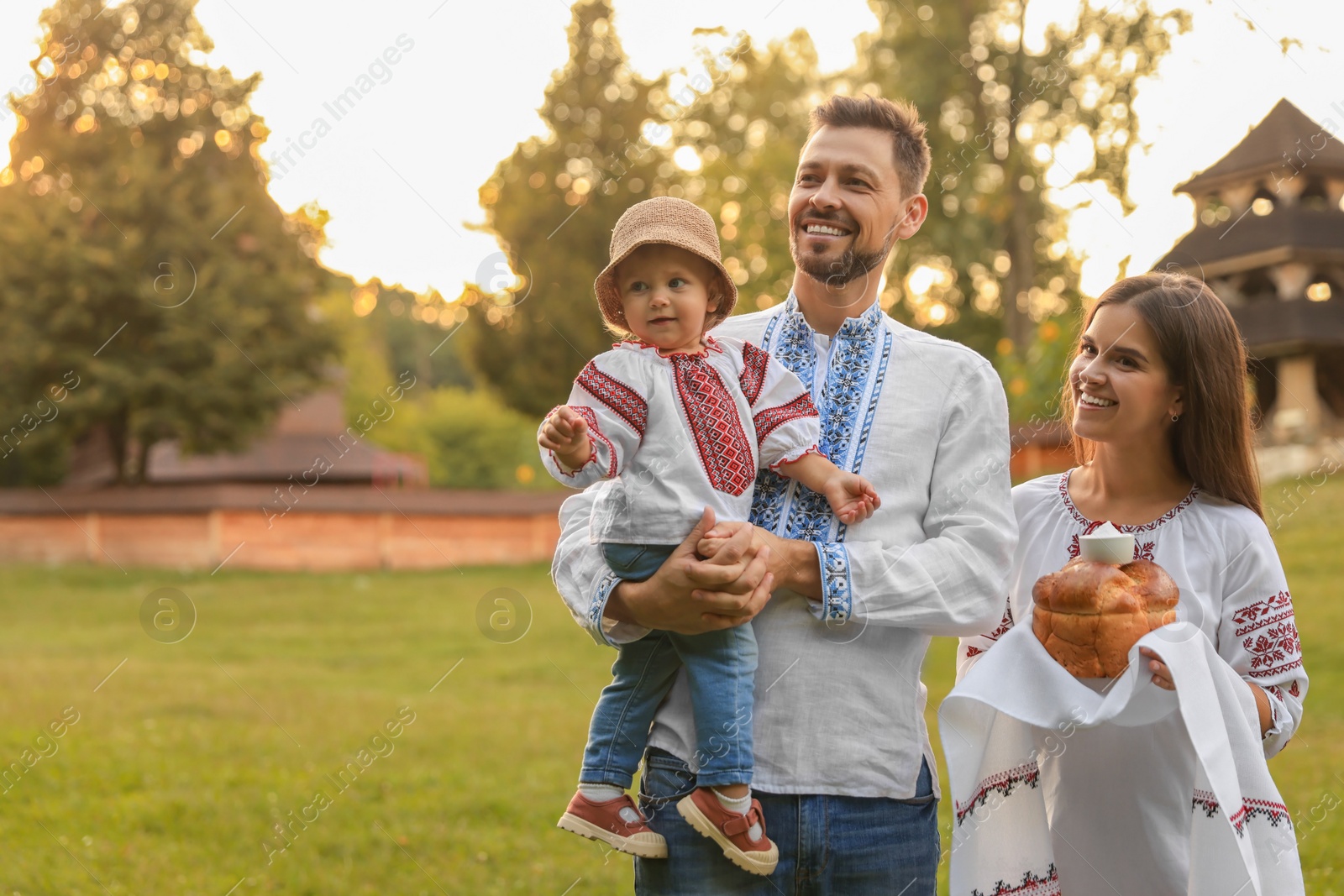 Photo of Happy cute family in embroidered Ukrainian shirts with korovai bread on sunny day. Space for text