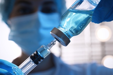 Photo of Woman filling syringe with vaccine from vial on blurred background, closeup