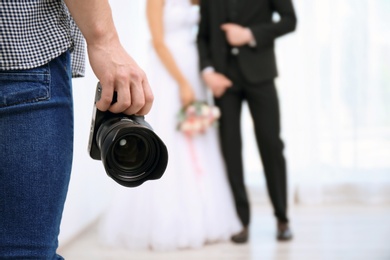 Photo of Professional photographer with camera and wedding couple in studio