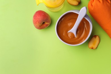 Photo of Healthy baby food in bowl and fresh peaches on light green background, flat lay. Space for text