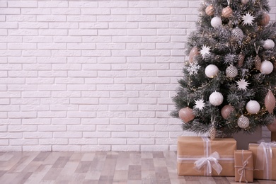 Photo of Beautifully decorated Christmas tree and gift boxes near white brick wall, space for text