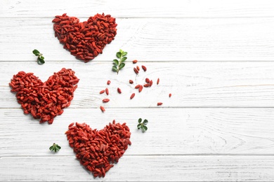 Photo of Hearts made of dried goji berries on white wooden table, flat lay with space for text. Healthy superfood