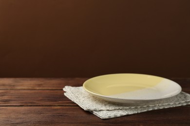 Photo of Beautiful ceramic plate and napkin on wooden table against brown background, space for text