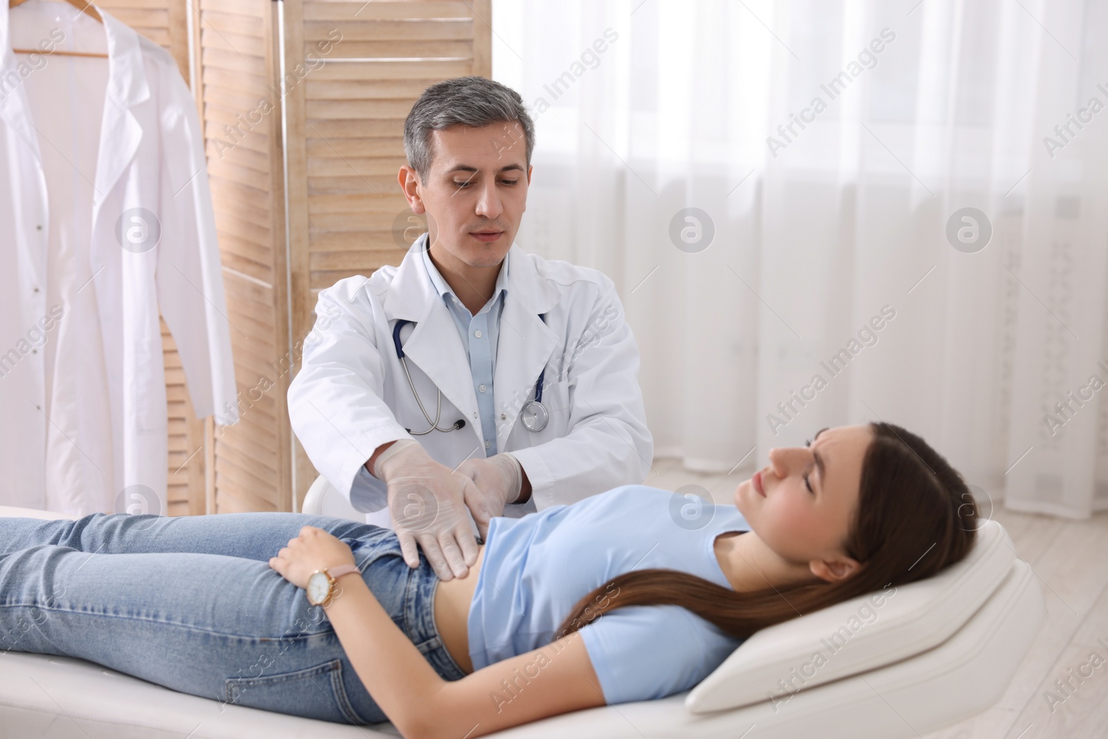 Photo of Gastroenterologist examining patient with stomach pain on couch in clinic