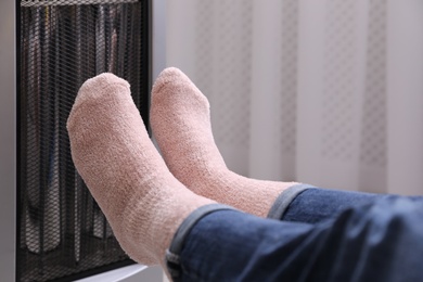 Photo of Woman warming feet near heater indoors, closeup