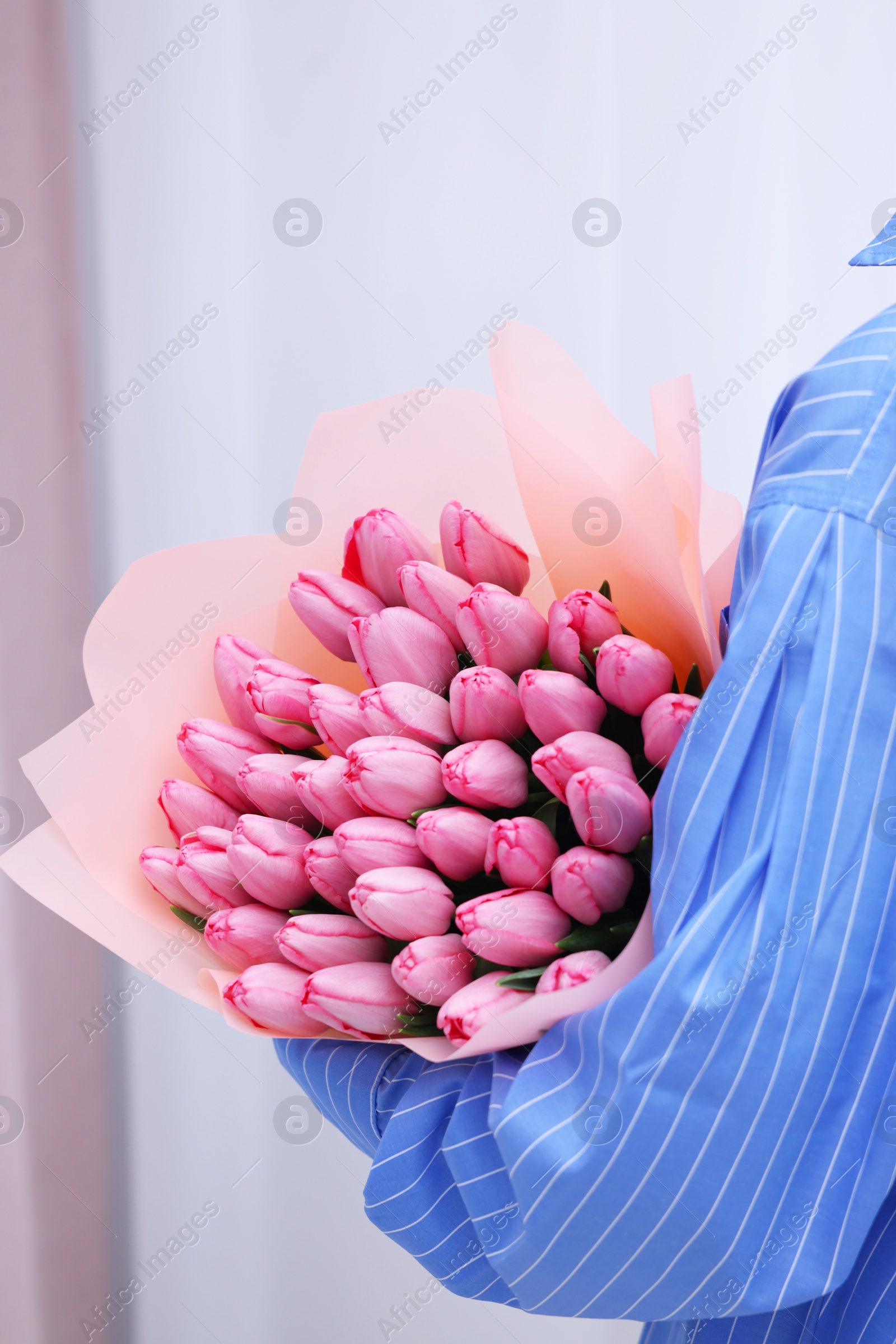 Photo of Woman holding bouquet of pink tulips indoors, closeup