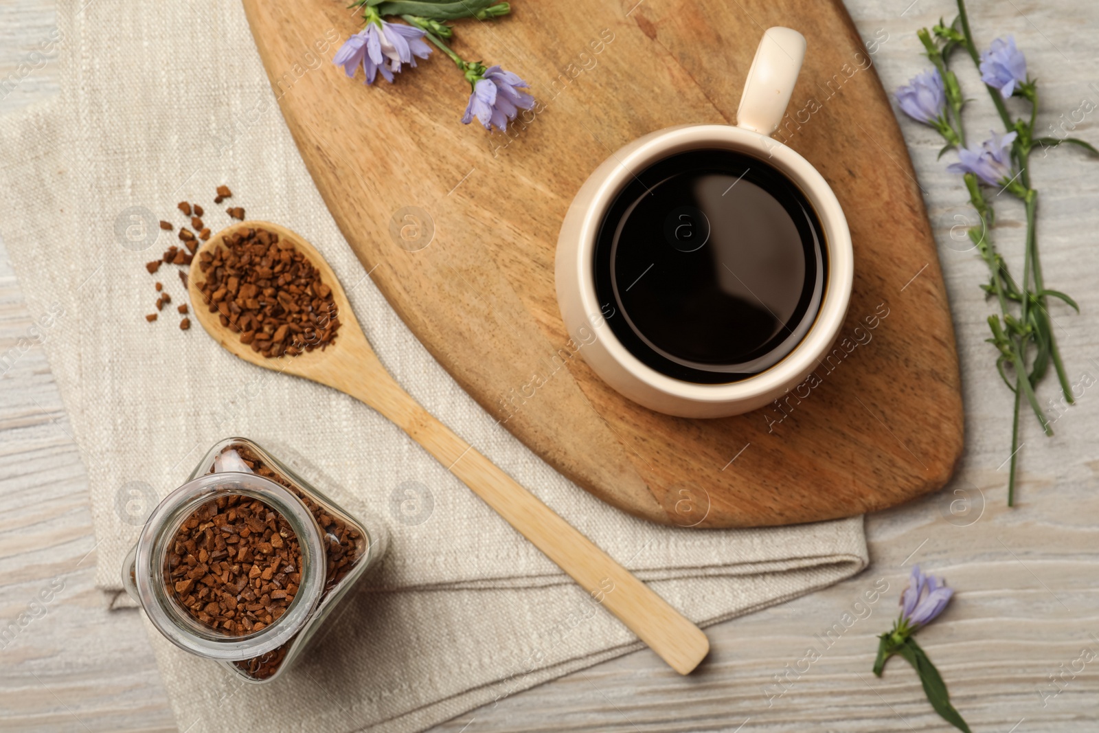 Photo of Cup of delicious chicory drink, granules and flowers on white wooden table, flat lay