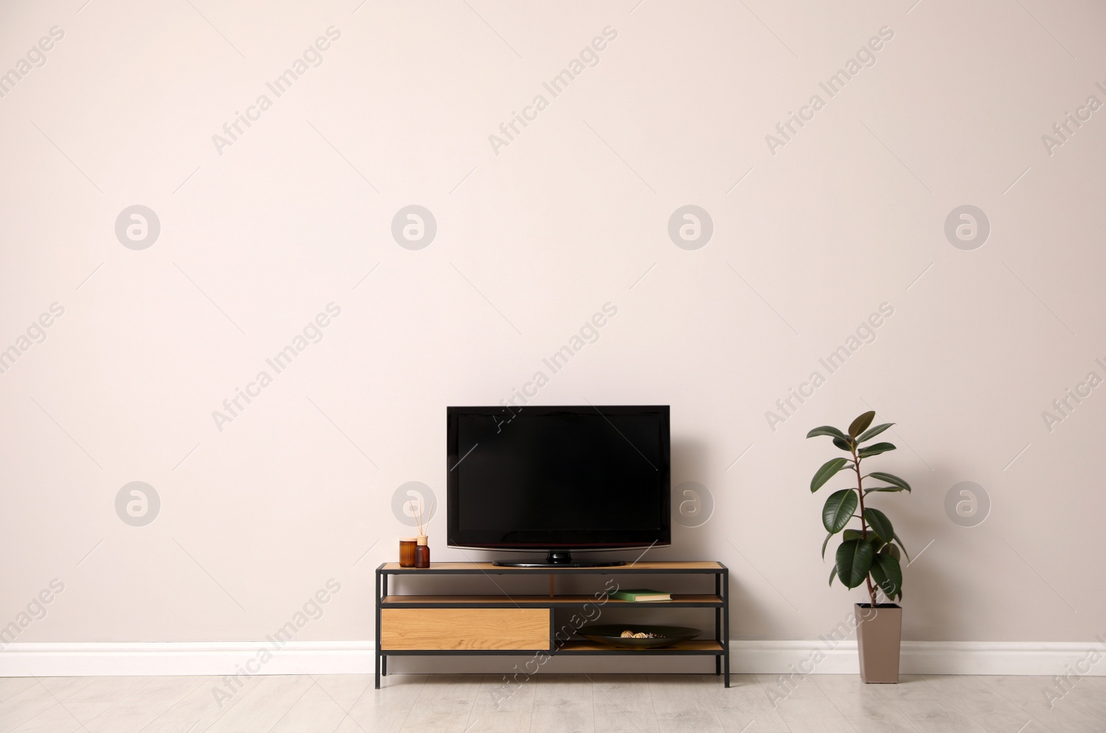 Photo of Elegant room interior with TV on cabinet and houseplant near light wall