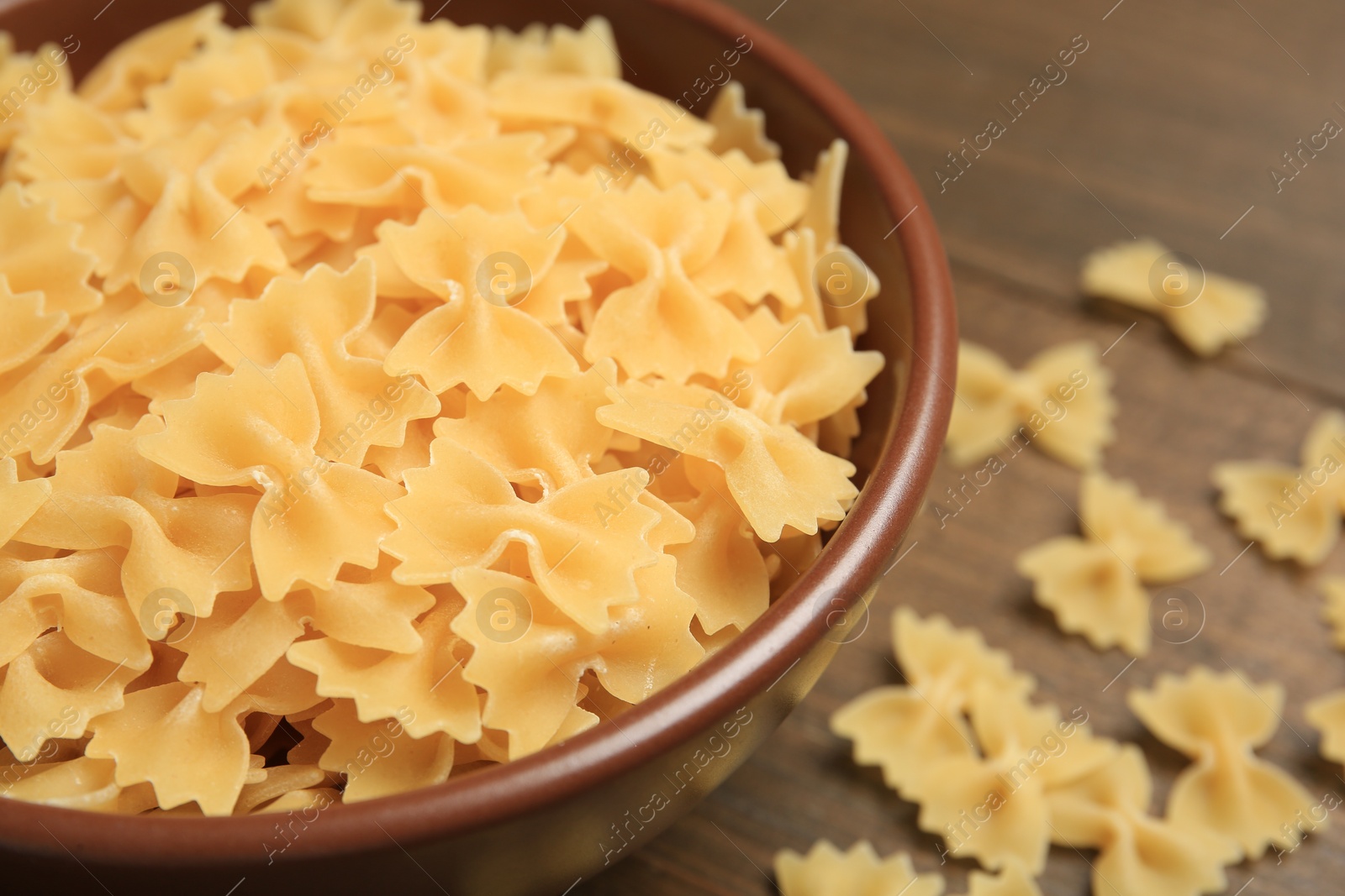Photo of Raw farfalle pasta in bowl on table, closeup